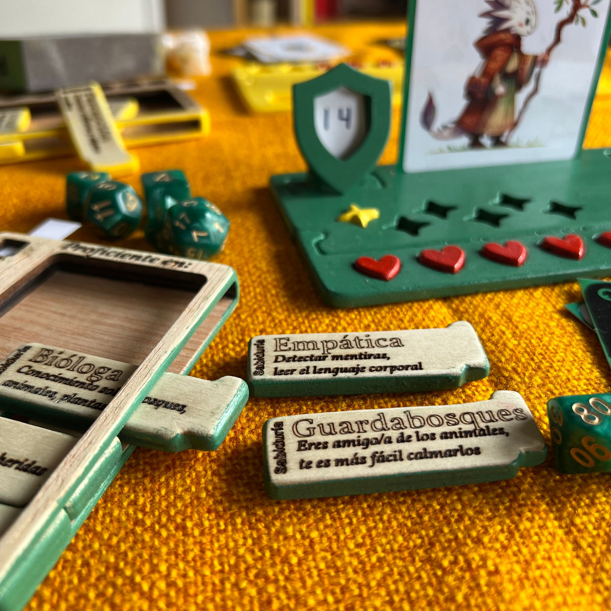 Materiales de juego de La Tarasca: cajas de madera, corazones rojos, cartas ilustradas, dados
